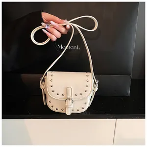 Detail view of mini saddle bag with silver rivets and metal ring on white faux leather