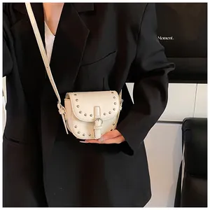 Detail view of white mini saddle bag with metal rivets and crossbody strap on black blazer