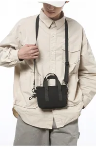 Detail view of a black canvas crossbody bag with nylon handles and adjustable strap