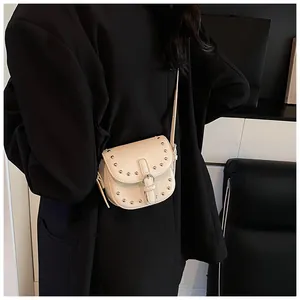 Detail shot of mini cream saddle bag featuring silver rivets and metal buckle on faux leather