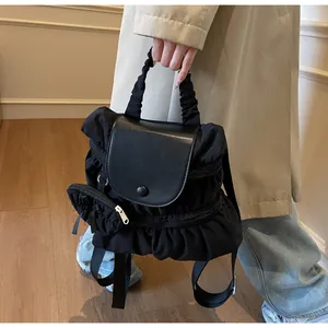 Detail of black pleated nylon backpack featuring a matte leather flap and matching pouch