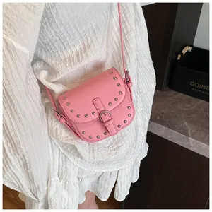 Detail of pink PU leather saddle bag with silver studs and pin buckle on a white dress