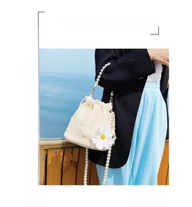 Detail of straw bucket bag with pearl handle, daisy ornament and long strap for summer