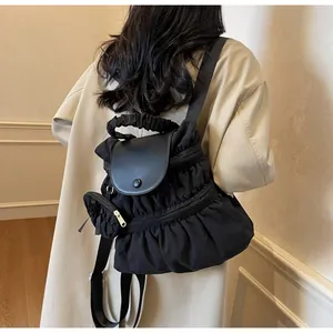 Detail of black pleated nylon backpack with leather flap worn by model in beige trench coat