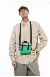 Detail of vibrant green canvas crossbody bag with adjustable black strap on a model
