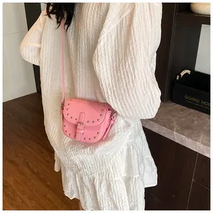 Detail of pink mini saddle bag with silver studs and buckle worn by model in white dress