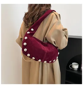 Close-up of burgundy suede underarm bag with silver stud rivets worn with a trench coat