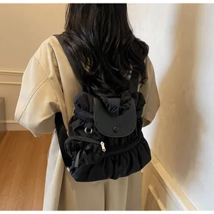 Close-up of black pleated nylon backpack with leather flap and snap button on model