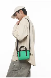Detail shot of a small green nylon crossbody bag showing dual handles and adjustable strap