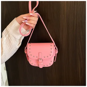 Close-up of pink mini saddle bag with silver studs and metal buckle on wooden wall