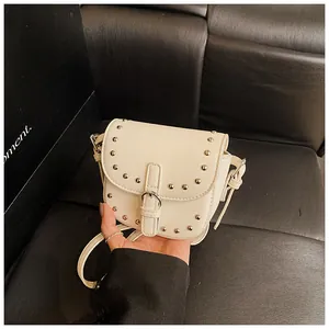 Detail view of cream white mini saddle bag with silver metal studs and buckle strap