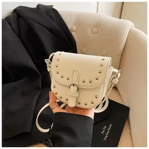 Detail of white mini saddle bag with silver studs and buckle against a vintage background