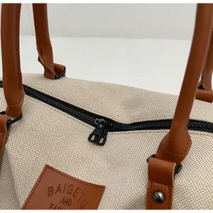 Close-up detail of beige canvas travel bag with brown leather handles and brand logo