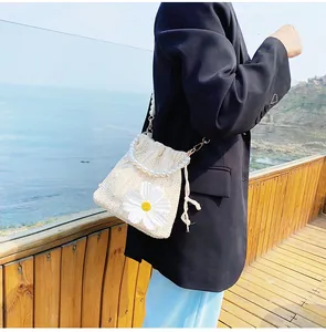 Detail of straw bucket bag with white daisy decor and elegant pearl chain handle