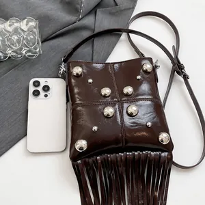 Detalle de bolso en cuero aceitado marrón con remaches plateados y flecos largos