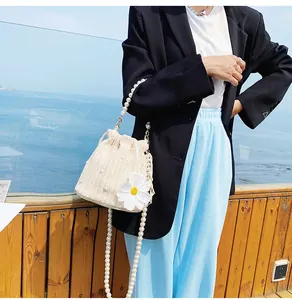 Detailed view of woven straw bucket bag with large white daisy flower and pearl chain strap