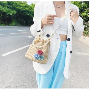 Detail of woven straw bucket bag featuring colorful floral appliques and pearl strap