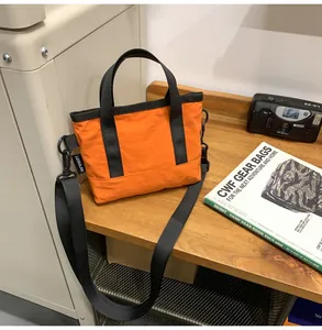 Detailed close-up of a lightweight orange nylon tote bag on a wooden table with accessories