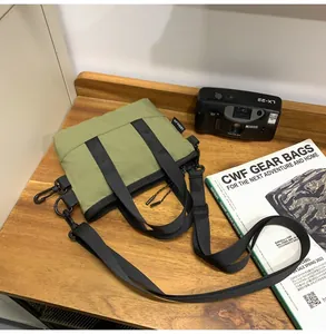Olive green canvas crossbody bag with nylon handles on a wooden table with camera