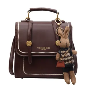 Bolso bandolera vintage marrón oscuro con costuras blancas y amuleto de conejo