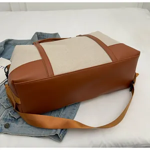 Detail of a beige canvas travel bag with brown faux leather trim and wide shoulder strap