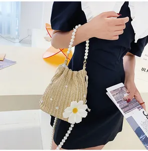 Detail view of straw bucket bag with pearl chain and white daisy floral accent