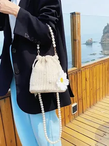 Elegant woven bucket bag with pearl strap and daisy floral detail on beach balcony