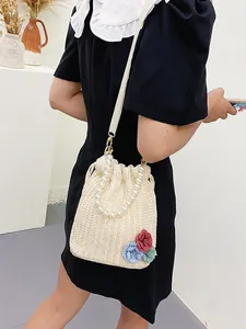 Straw woven beach bag with pearl handle and 3D floral accents worn by a model