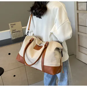 Rear view of a model carrying a large canvas and brown leather travel tote bag in a warm room