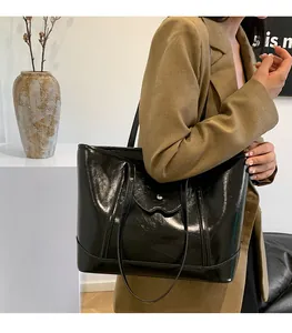 Detail of a large black glossy tote bag with silver buckle and mirror finish texture