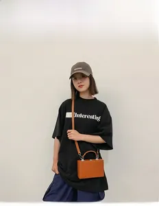 Detail shot of orange hard shell crossbody box bag worn with casual streetwear outfit