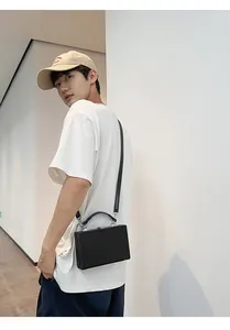 Male model wearing a black hard shell box bag with silver hardware and a thin shoulder strap