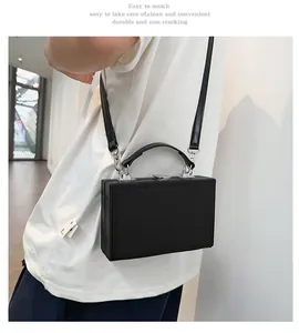 Detail of a black hard-shell box bag worn crossbody by a model in a minimal setting