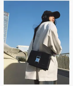 Detail of a black leather crossbody bag with a large silver buckle in an urban street setting