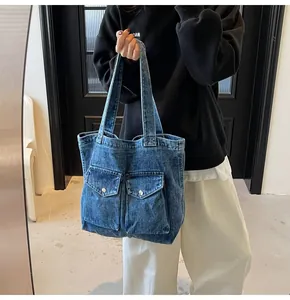 Détail du sac cabas en jean bleu avec deux poches avant et boutons métalliques