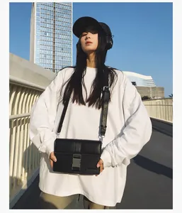 Close-up of black leather rectangular crossbody bag with silver buckle in street setting