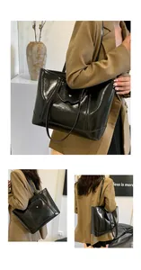 Detail of a large black glossy leather tote bag with a unique wavy flap and metal accents