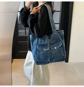 Modèle portant un grand sac cabas en jean bleu foncé avec deux poches à boucles