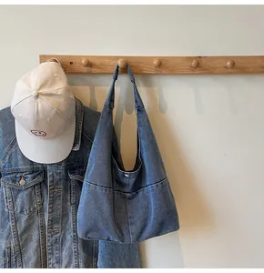 Detail of blue denim shoulder bag showing stitching texture with cap on wall hook