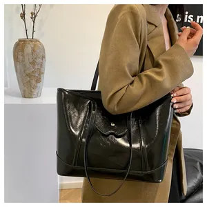 Detail of glossy black tote bag featuring wave-shaped flap and metallic silver button