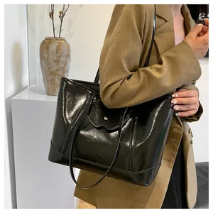 Detail of glossy black tote bag featuring metallic buckle and horse-embossed flap