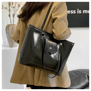 Side view of a black glossy large tote bag worn by a model in a minimalist studio