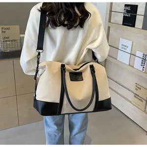 Detail of a beige canvas duffle bag with black leather trim and adjustable strap