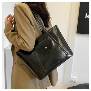 Detail of glossy black tote bag with silver rivet and long straps on woman shoulder