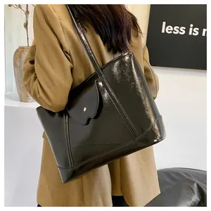 Minimalist black patent leather tote bag with metallic buckle pocket worn by a model