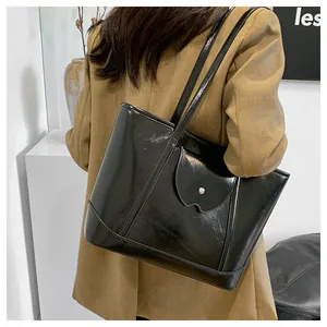 Model wearing a glossy black tote bag with wavy flap detail and metal buckle