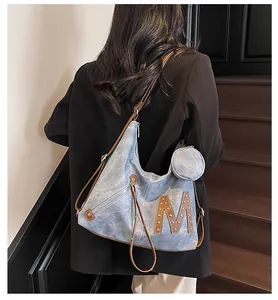 Detail of blue denim tote bag with brown leather M patch, rivets and mini coin purse