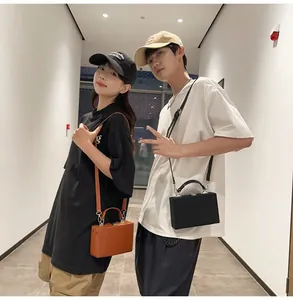 Street style couple holding compact hardshell box bags in black and brown leather