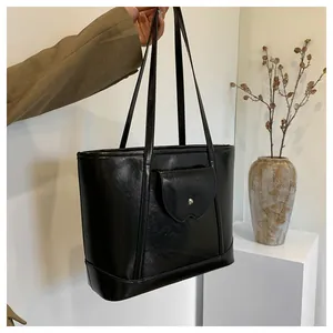 Detailed side view of black faux leather tote bag with slender straps and front pocket
