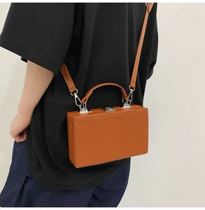Detail of a brown hard-shell box bag with silver hardware and a top handle